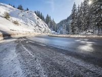 a mountain road with no vehicles or traffic is covered in snow and ice with pine trees in the background