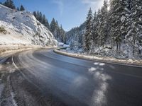 a mountain road with no vehicles or traffic is covered in snow and ice with pine trees in the background