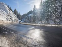 a mountain road with no vehicles or traffic is covered in snow and ice with pine trees in the background