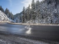 a mountain road with no vehicles or traffic is covered in snow and ice with pine trees in the background