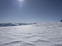 there is a very big expanse of snow and a bright sun above the mountain tops