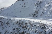 a person riding on top of snow covered mountains down a road and another riding the side