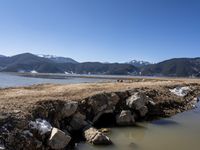 mountains with snow covered rocks sitting in the water next to a shore line and some water