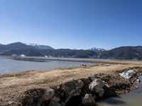 mountains with snow covered rocks sitting in the water next to a shore line and some water