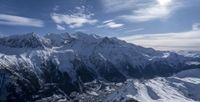 a view of a valley with snow covered mountains in the distance, and clouds in the sky above