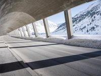 view from inside a curved bridge towards snow covered mountains in the distance with snow piles on either side