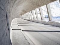 view from inside a curved bridge towards snow covered mountains in the distance with snow piles on either side