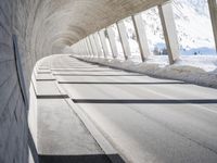 view from inside a curved bridge towards snow covered mountains in the distance with snow piles on either side