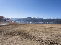 a dry field with many wind generators in the background and snow covered mountains on either side