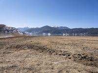 a dry field with many wind generators in the background and snow covered mountains on either side