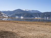 a dry field with many wind generators in the background and snow covered mountains on either side