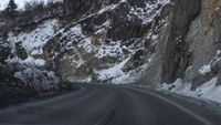 a narrow road that is covered by snow and rock formations with a mountain behind it