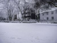 a person is walking through the snow covered park in front of a building with a white porch