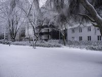 a person is walking through the snow covered park in front of a building with a white porch