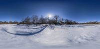 a wide angle photo of the sun in the snow outside of a farmyard and trees