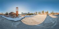 the camera is taking a photo of a snow covered park area with benches and a tower