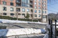 the parking meter on the sidewalk in front of some buildings with snow on it and a fence