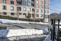 the parking meter on the sidewalk in front of some buildings with snow on it and a fence