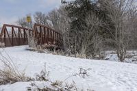 a snow covered ground with a bridge and trees in the background on a winter day