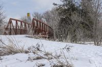 a snow covered ground with a bridge and trees in the background on a winter day