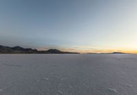 snow covered plain with several footprints in it, with mountain and sky behind it in background