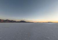 snow covered plain with several footprints in it, with mountain and sky behind it in background