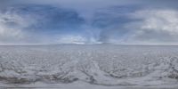 a cloud is coming off an overcast sky with a view across the field to a large, distant snow covered plain