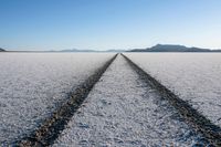 the dirt road leading to the mountains in the middle of a snow field, near salt flat plains