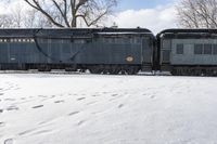 an old style train is on the tracks in snow next to some trees and blue skies