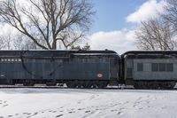 an old style train is on the tracks in snow next to some trees and blue skies