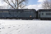 an old style train is on the tracks in snow next to some trees and blue skies