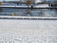 a fire hydrant near the edge of a river covered in snow next to a dock