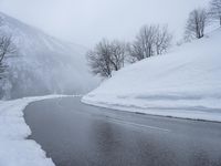 the road is covered in snow at the foot of a mountain slope that is steep