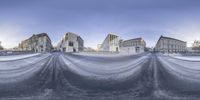 snow covers a road with lots of buildings in the background in the winter time,