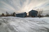 a road with snow and two old barn buildings in the background are a few others in this shot