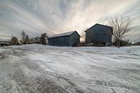 a road with snow and two old barn buildings in the background are a few others in this shot