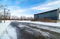 snow sits on the side of the road in front of a barn and power lines