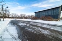 snow sits on the side of the road in front of a barn and power lines