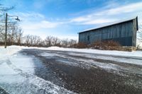 snow sits on the side of the road in front of a barn and power lines