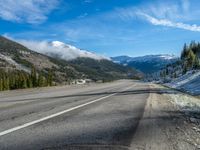 a car drives through the snow near a wooded mountain side road with rolling clouds hovering above the mountains