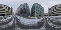 a snow covered road near a parking lot, a building with many windows next to it