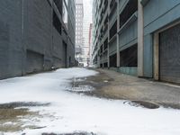 the view up an empty alley in a city with snow on the ground and buildings in the distance