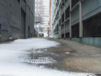 the view up an empty alley in a city with snow on the ground and buildings in the distance