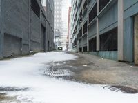 the view up an empty alley in a city with snow on the ground and buildings in the distance