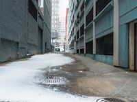 the view up an empty alley in a city with snow on the ground and buildings in the distance