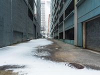 the view up an empty alley in a city with snow on the ground and buildings in the distance