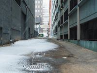 the view up an empty alley in a city with snow on the ground and buildings in the distance