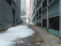 the view up an empty alley in a city with snow on the ground and buildings in the distance