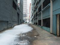 the view up an empty alley in a city with snow on the ground and buildings in the distance