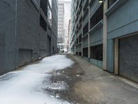 the view up an empty alley in a city with snow on the ground and buildings in the distance